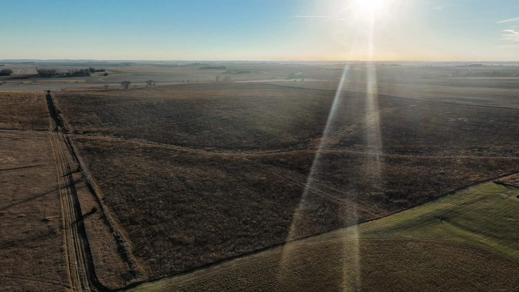 a bird's eye view of farmland in Butler County, Iowa. The sky is clear and the sun is shining ray onto the land.