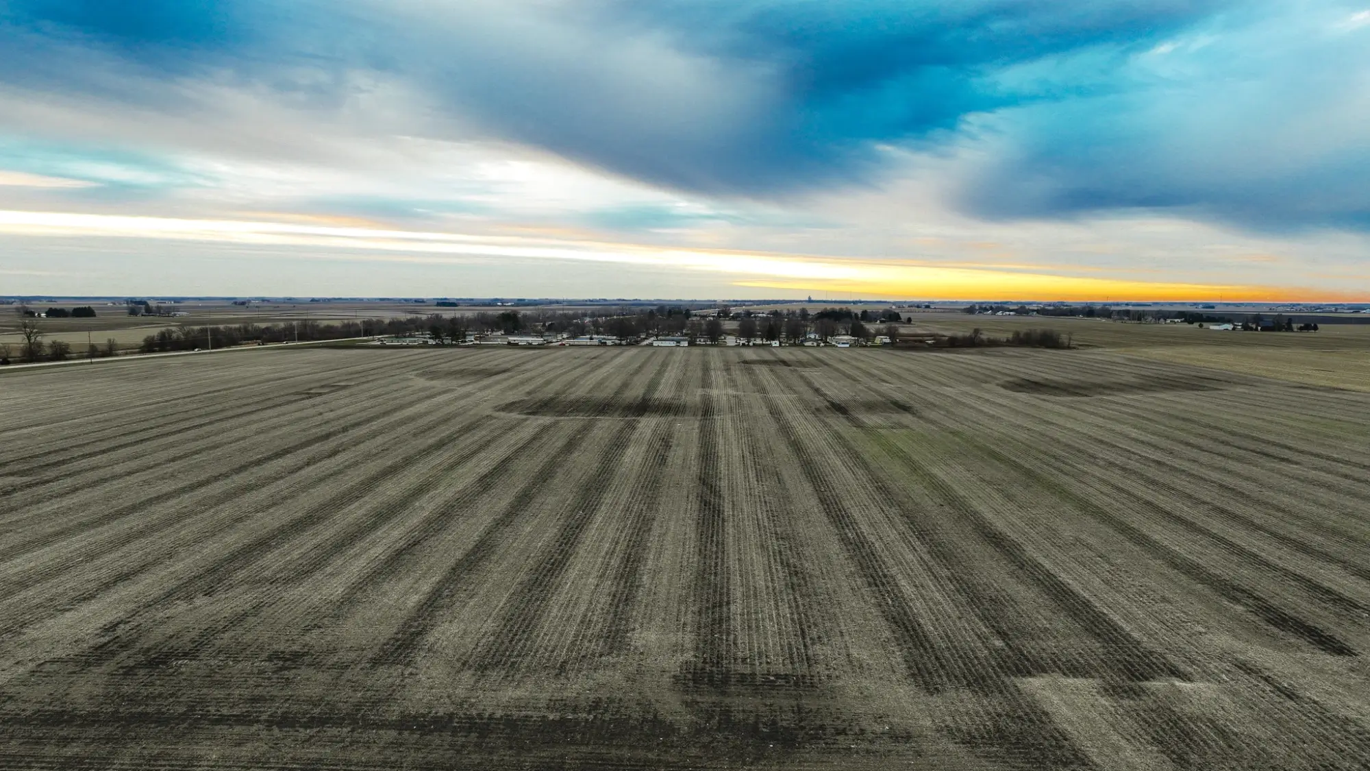 a bird's eye view of farmland in Champaign County, Illinois. The sky is cloudy and the sun is setting.