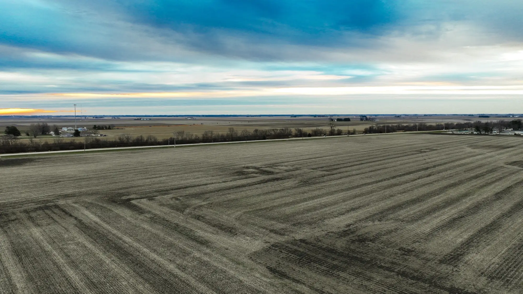 a bird's eye view of farmland in Champaign County, Illinois. The sky is cloudy and the sun is setting.