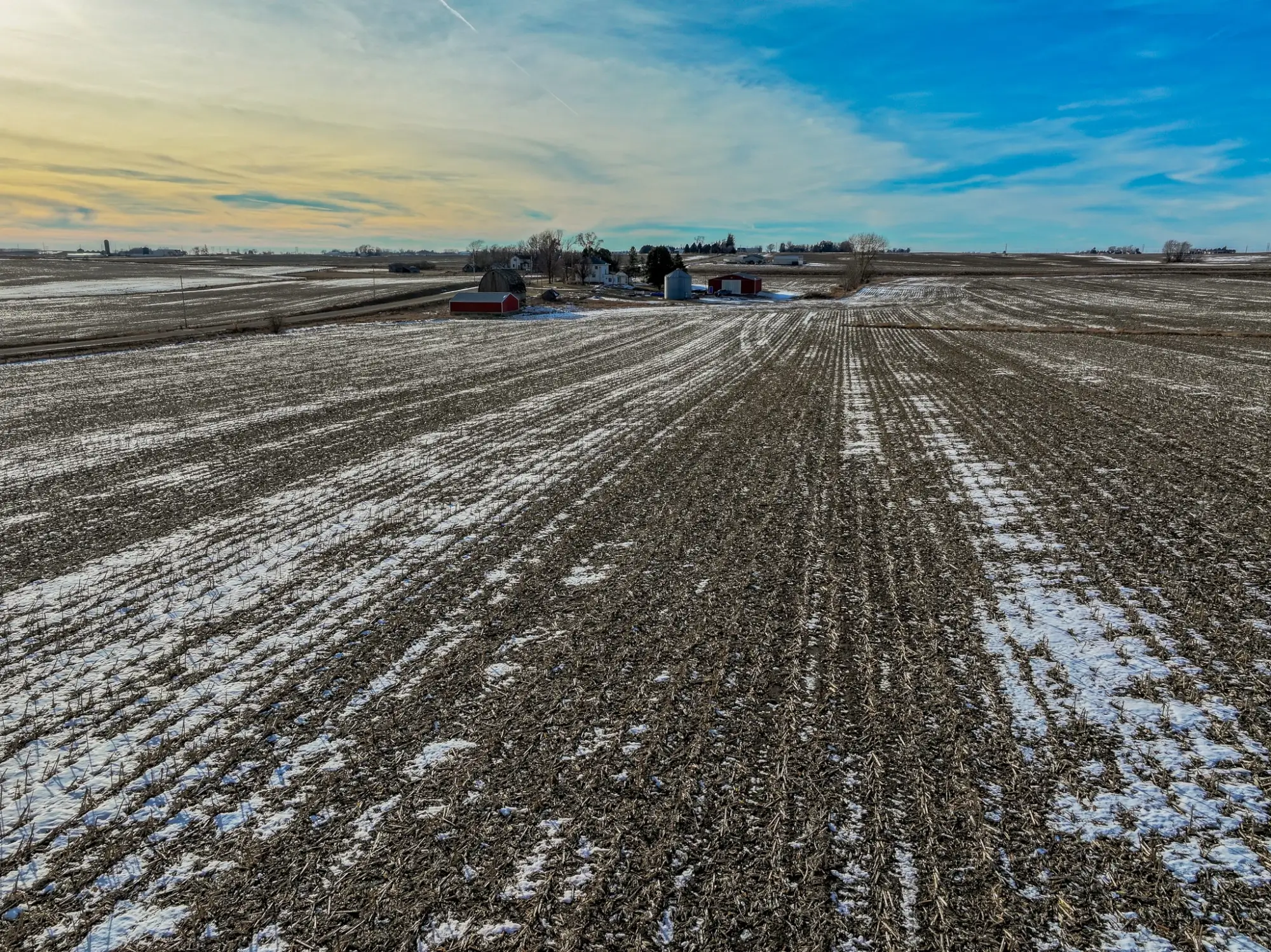 a photo of a bird's eye view of Boone County, Iowa farmland. The sky is bright blue with a hint of orange with a few clouds.
